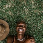 Portrait Of A Beautiful Black Woman Smiling & Laying Down In The Grass.